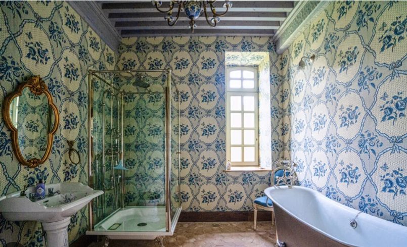 A bathroom papered in blue, a claw-foot bath beneath the window