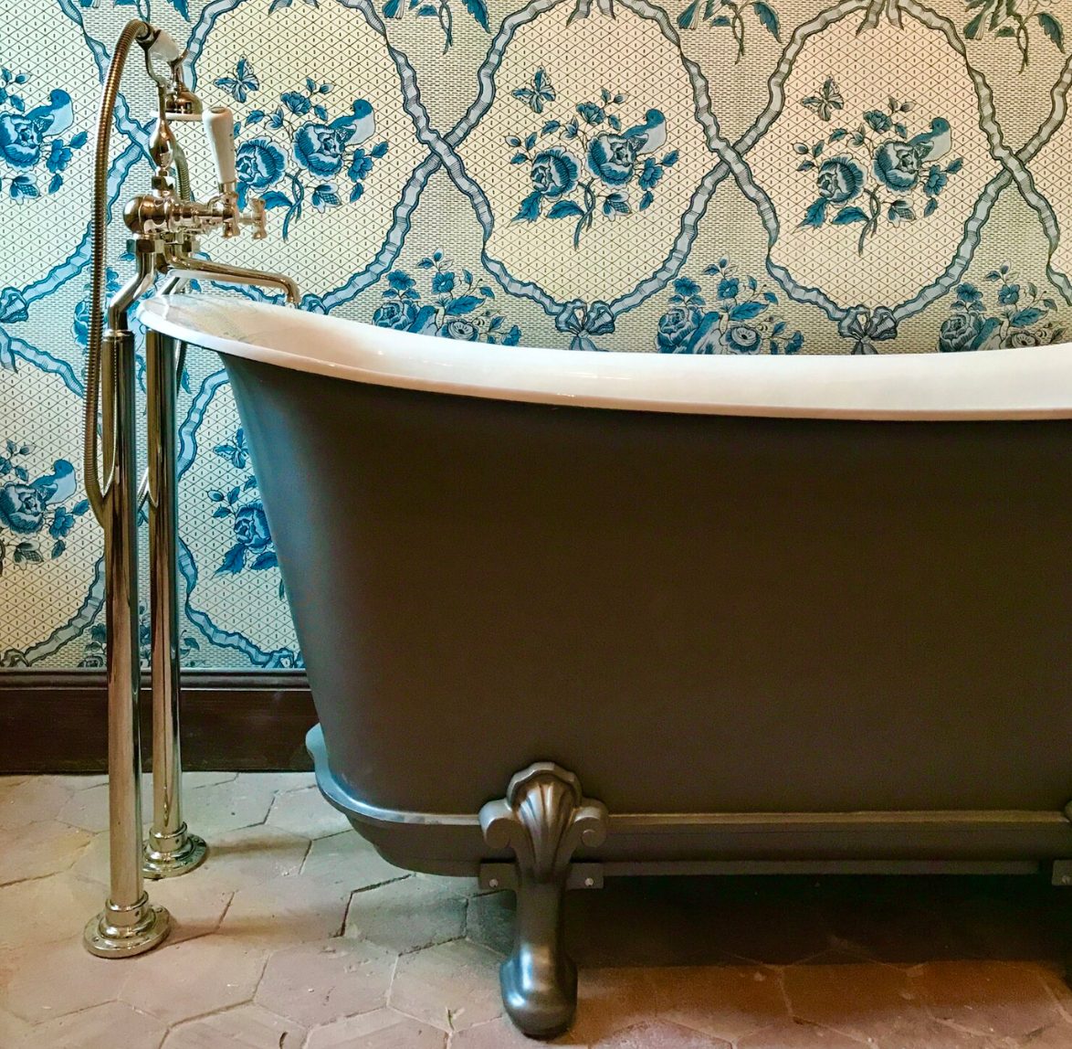 A bathroom papered in blue, the claw-foot bath on the old terracotta