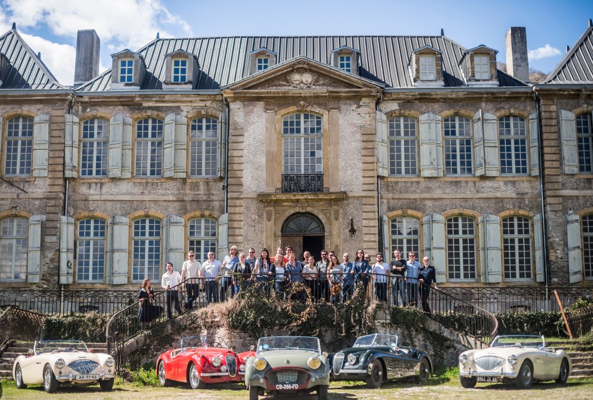 A classic car club gathered on the steps, their cars before the château